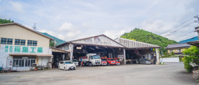 緑に囲まれた山間部の整備工場の外観。複数の車両が整備されている様子。